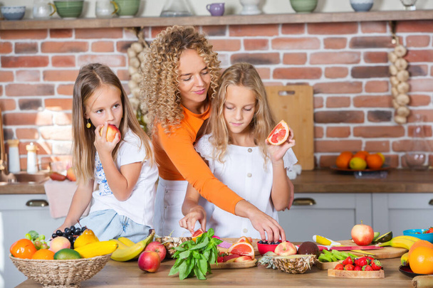 Madre e hijas cocinando juntas en la cocina. Concepto de comida saludable. Retrato de familia feliz con batidos frescos. - Foto, imagen