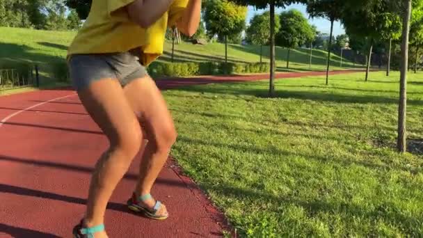 A fiatal nő intenzív láb- és combedzésre indul egy napsütéses reggelen egy nyilvános parkban. A közeli női alsó rész természetes izommozgást mutat, ahogy a gyakorlatba kezd. - Felvétel, videó