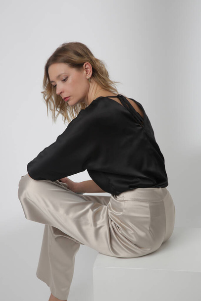Série de fotos de estúdio de jovem modelo feminino vestindo roupas bonitas simples, blusa preta de cetim de seda e calças brancas de perna larga - Foto, Imagem