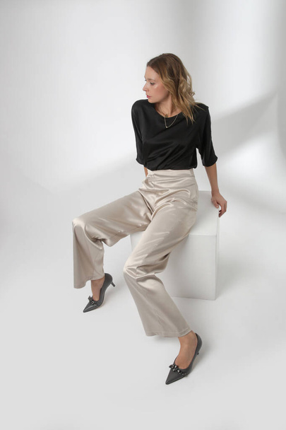 Serie of studio photos of young female model wearing simple beautiful outfit, silk satin black blouse and white wide leg trousers - Φωτογραφία, εικόνα