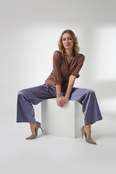 Serie de fotos de estudio de la joven modelo femenina con un traje hermoso simple, blusa de satén marrón de seda y pantalones de pierna ancha lila - Foto, Imagen