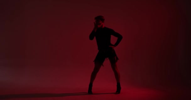 A silhueta impressionante de uma dançarina de ascendência caucasiana, vestida com uma saia de couro, realiza uma dança encantadora contra um pano de fundo vermelho. Sua dança, realçada pelo contraste entre luz e sombra. - Filmagem, Vídeo