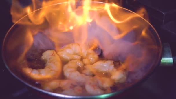 Primer plano cámara lenta de la preparación de camarones con ajo en sartén de metal con llama ardiente en la cocina del restaurante - Metraje, vídeo