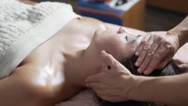 Žena se zavřenýma očima ležící na gauči při relaxaci při masáži obličeje anonymním masérem - Záběry, video