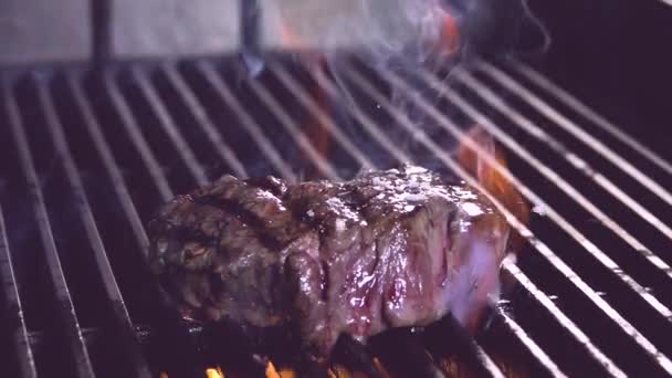 Detailní pomalý pohyb vařeného masového steaku umístěného na kovovém roštu na pánvi s hořícím plamenem - Záběry, video