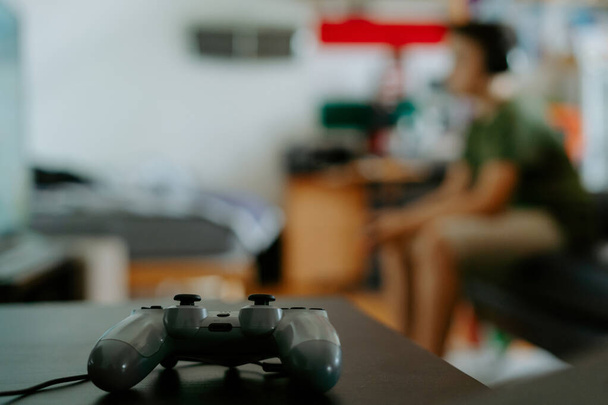 De cima gamepad moderno para jogos de vídeo colocados na mesa na sala contra menino irreconhecível sentado no sofá - Foto, Imagem
