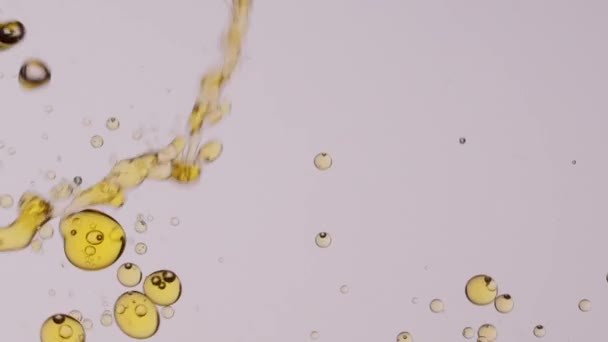 Gros plan mouvement lent de l'huile jaune étant versé dans l'eau transparente et formant de nombreuses bulles flottantes pour le fond abstrait - Séquence, vidéo