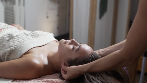 Зверху жінка з закритими очима лежить на дивані, розслабляючись під час масажу обличчя анонімним масажистом - Кадри, відео
