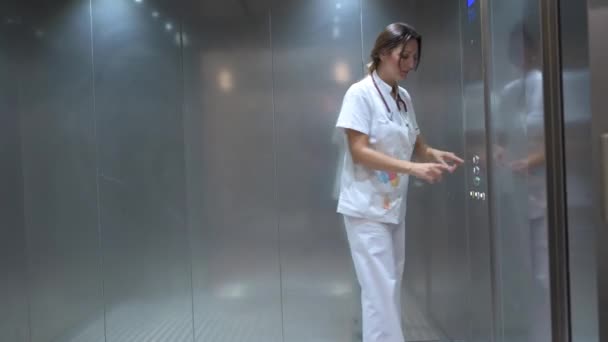 Koko kehon nainen valkoisessa lääketieteellisessä univormussa painike hissin sisällä työskennellessään sairaalassa - Materiaali, video