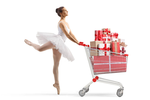 Full length profile shot of a ballerina dancing and pushing a shopping cart with presents isolated on white background - Valokuva, kuva