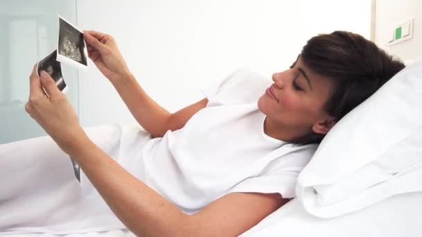 Από πάνω έγκυος γυναίκα επιθεώρηση υπερηχογράφημα εικόνα, ενώ βρίσκεται στο κρεβάτι σε θάλαμο της σύγχρονης κλινικής γονιμότητας - Πλάνα, βίντεο
