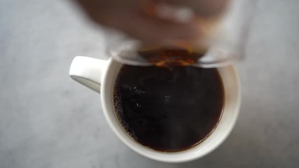 Crop anonieme vrouw gieten verse hete gebrouwen koffie uit glazen kan in beker in gezellige keuken thuis - Video