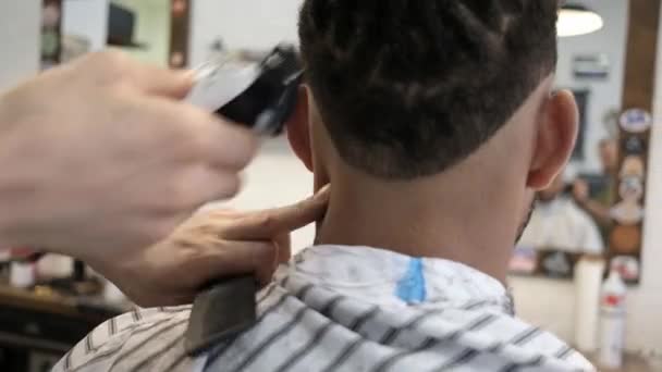 Vista de las cosechas por detrás del estilista anónimo haciendo un corte de pelo moderno con una navaja de afeitar a un cliente afroamericano sin rostro - Imágenes, Vídeo