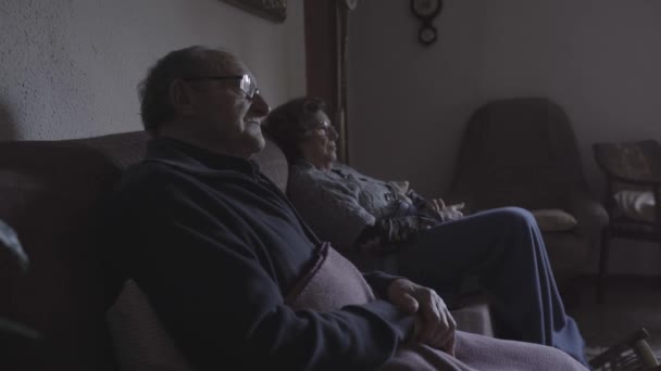 Vista laterale della coppia anziana seduta sul divano a casa mentre guarda la tv - Filmati, video
