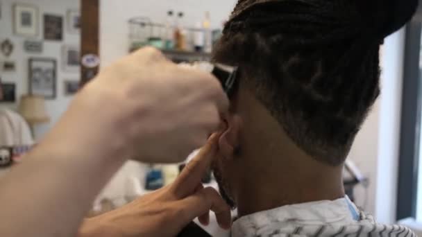 Widok na zboże z tyłu anonimowy fryzjer robi nowoczesną fryzurę z brzytwą do bezimiennego klienta afro-amerykańskiego - Materiał filmowy, wideo