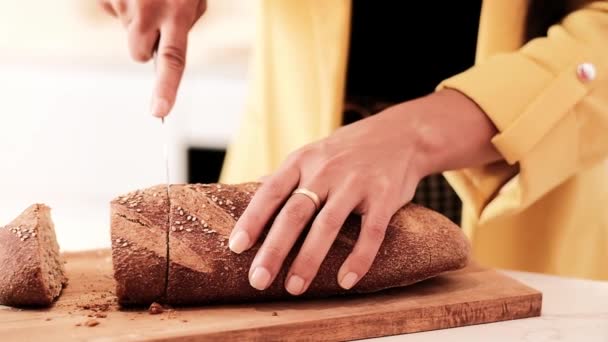 Crop női elegáns ruhát áll konyhaasztal és a vágás kenyér - Felvétel, videó