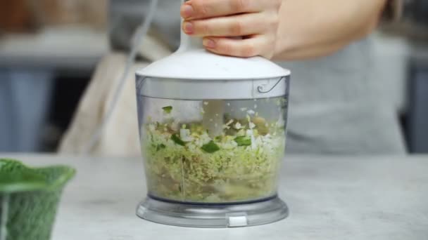 Nerozpoznatelná žena pomocí mixéru krájet čerstvý česnek a zelenou cibuli při přípravě oběda v kuchyni doma - Záběry, video