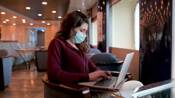Serious female freelancer in protective mask sitting on board of cruise ship and typing on netbook while working on new project - Footage, Video
