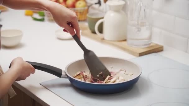 Uprawa nierozpoznawalna samica dodająca olej podczas mieszania krojonych grzybów i cebuli z smażeniem szpatułki na patelni podczas przygotowywania obiadu w kuchni - Materiał filmowy, wideo