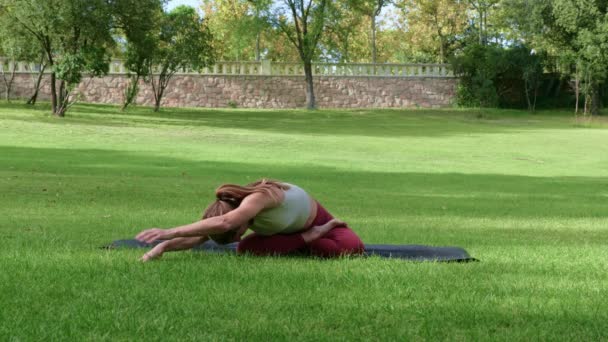 Real time of young sportive female in sports wear sitting in Sukhasana on mat while doing right and left forward bend stretch and sklon back - Záběry, video