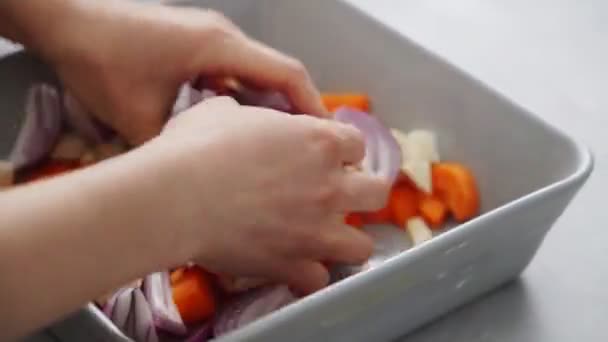 Hoher Winkel der anonymen weiblichen Mischung geschnitten Karotten und Zucchini mit Zwiebeln in Keramik Backform beim Kochen vegetarisches Mittagessen - Filmmaterial, Video