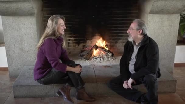 Vue latérale de couple âgé aimant assis près de la cheminée et tenant la main tout en se reposant ensemble dans une chambre confortable de la maison de campagne - Séquence, vidéo