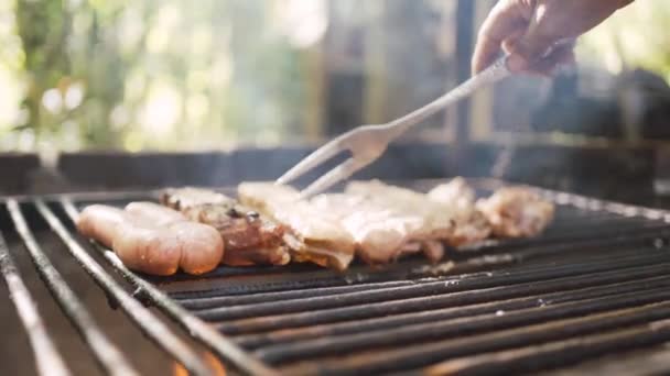 Recadré mains personne méconnaissable avec fourchette ajuster les morceaux de viande fraîche sur rack sur la flamme dans le jardin - Séquence, vidéo