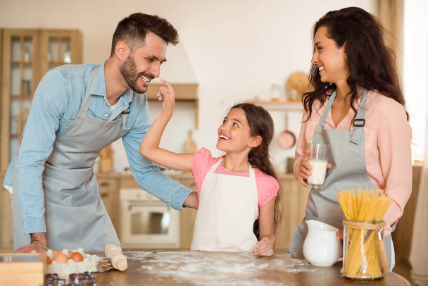 Nadšený dítě dívka hrát s podlahou a táta při pečení s rodiči společně v kuchyni. Šťastný otec, matka a preteen fena těší vaření doma - Fotografie, Obrázek