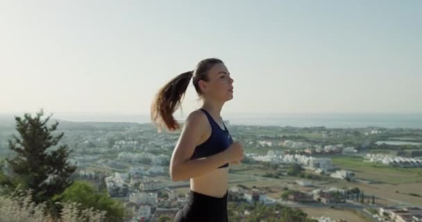 Een vrouw die jogt met uitzicht op het stadsgezicht. Sportief actief sportief meisje rennend in de bergen met uitzicht op de stad. Hoge kwaliteit 4k beeldmateriaal - Video