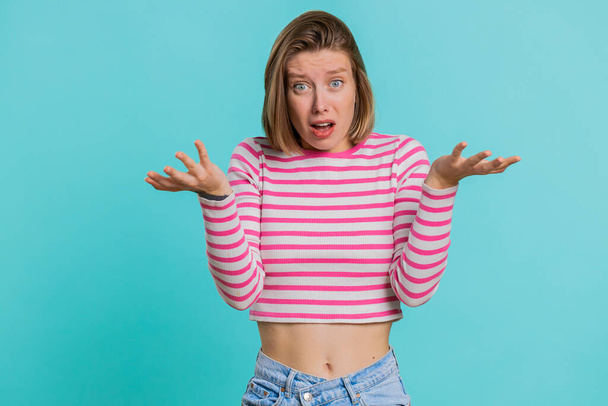What Why. Sincere irritated young woman raising hands in indignant expression, ask reason of failure demonstrating disbelief irritation by trouble. Pretty confused girl in crop top on blue background - Photo, Image