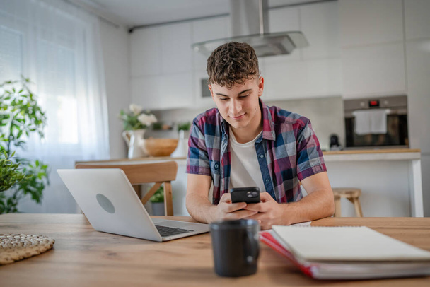Jovem caucasiano homem adolescente estudante estudar em casa uso telefone celular smartphone mensagens SMS - Foto, Imagem