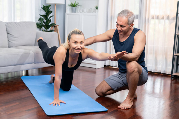 Boldog aktív idős pár a sportruházatban, akik támogatnak és segítenek a jóga testtartásban otthon. Egészséges idős férfi és nő életmód jóga gyakorlattal. Kömény - Fotó, kép