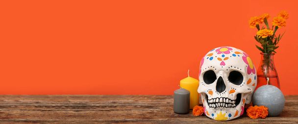 Painted human skull for Mexico's Day of the Dead (El Dia de Muertos), candles and flowers on table against orange background with space for text - Photo, Image