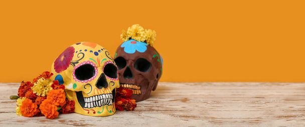 Painted human skulls for Mexico's Day of the Dead (El Dia de Muertos) and flowers on table against orange background with space for text - Photo, Image