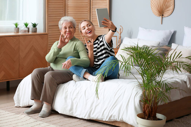 Mujer joven con su abuela usando tableta en el dormitorio - Foto, imagen