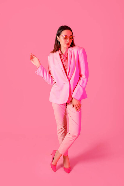 Νεαρή γυναίκα με κομψό κοστούμι σε ροζ φόντο - Φωτογραφία, εικόνα
