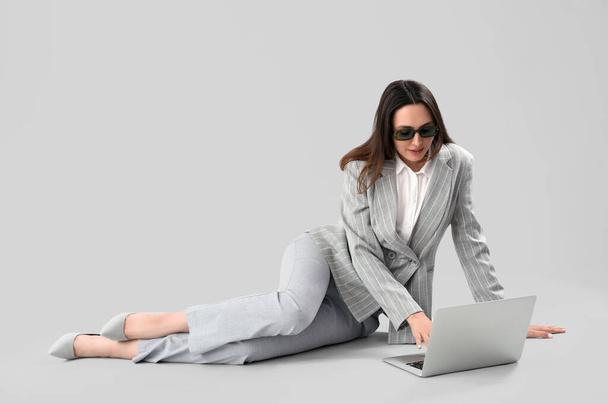 Fiatal üzletasszony stílusos öltöny segítségével laptop könnyű háttér - Fotó, kép