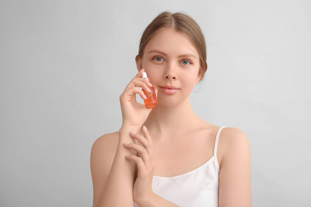 Hübsche junge Frau mit Kosmetiköl auf hellem Hintergrund - Foto, Bild