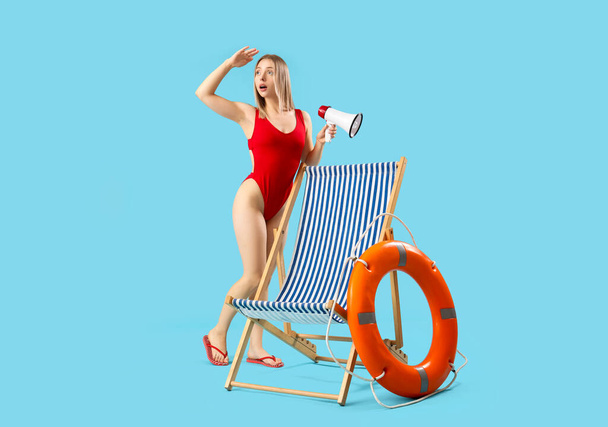 Beautiful woman with megaphone, deck chair and ring buoy on blue background - Photo, Image