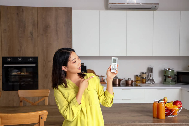 Belle femme asiatique allumant le climatiseur dans la cuisine - Photo, image