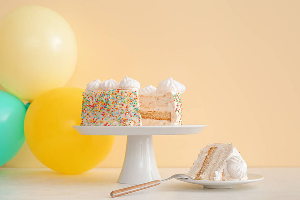 Ballons et stand avec délicieux gâteau d'anniversaire sur la table près du mur beige - Photo, image