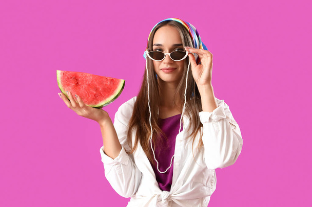 Молода жінка в сонцезахисних окулярах зі свіжим кавуном на фіолетовому фоні - Фото, зображення