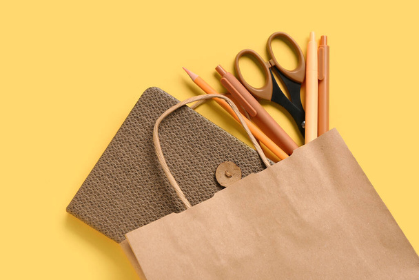 Paper bag with different stationery on yellow background, closeup - Photo, Image