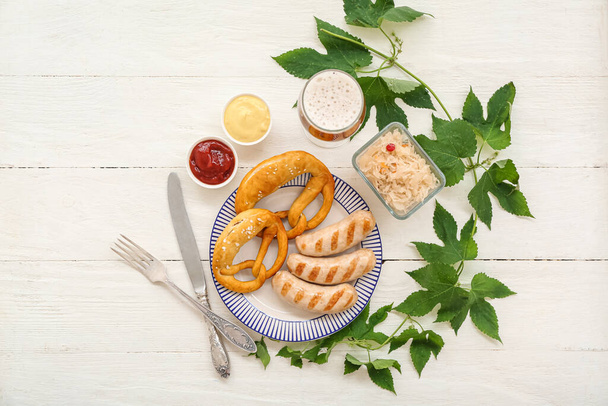 Тарілка зі смачними баварськими ковбасками, кренделями, соусами, квашеною капустою та келихом пива на білому дерев'яному фоні. святкування Октоберфесту - Фото, зображення