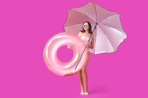 Belle jeune femme avec anneau gonflable et parapluie sur fond violet - Photo, image