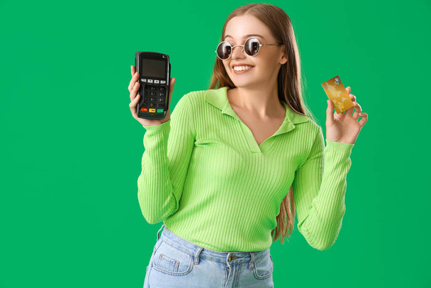 Junge Frau mit Kreditkarte und Zahlungsterminal auf grünem Hintergrund - Foto, Bild