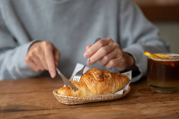 Image en gros plan d'un homme découpant un croissant avec une fourchette et un couteau, mangeant un délicieux croissant frais dans un café. Les gens et le concept alimentaire - Photo, image