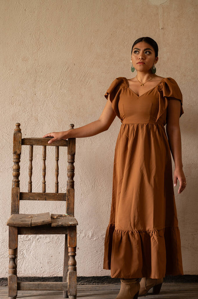 Frida-inspirierte Essenz: Eine mexikanische Frau, die an Frida Kahlo erinnert, ziert einen in die Jahre gekommenen Stuhl unter zarten Torbögen. Gebadet in einem Spiel von Licht und Schatten, ihrer traditionellen Kleidung und ihrem kontemplativen Blick - Foto, Bild