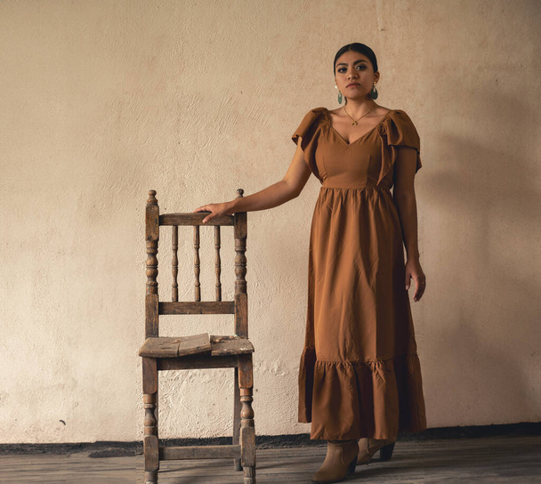Frida-Inspired Essence: Meksikolainen nainen, muistuttaa Frida Kahlo, armoa vuotiaiden tuoli alla herkkä väyliä. Kylvyssä valon ja varjon näytelmässä, hänen perinteinen pukunsa ja mietiskelevä katseensa - Valokuva, kuva