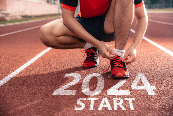 Neujahrskonzept 2024. Menschenhände binden Schnürsenkel-Laufschuhe und bereiten sich auf Ziele für 2024 vor. - Foto, Bild